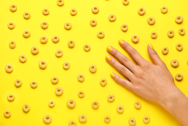 Woman with beautiful manicure and cereal rings on yellow background - Фото, изображение
