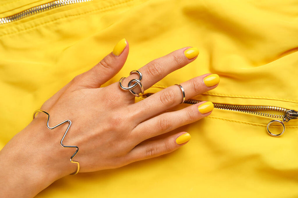 Vrouw met mooie manicure en stijlvolle sieraden op gele stof achtergrond - Foto, afbeelding