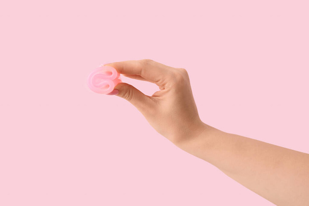 Naisten käsi kuukautiskierron kuppi vaaleanpunainen tausta - Valokuva, kuva