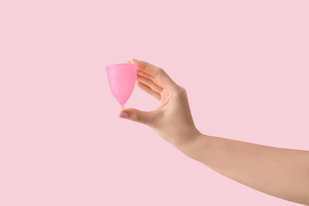 Mano femenina con copa menstrual sobre fondo rosa - Foto, imagen