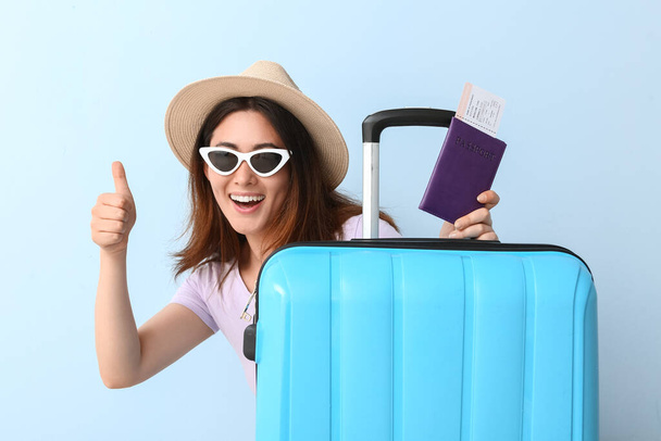 Young woman with passport and suitcase on color background - Фото, изображение