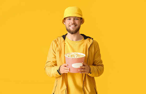 Young man with bucket of popcorn on color background - 写真・画像