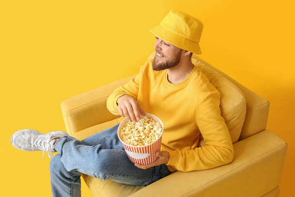 Uśmiechnięty facet z popcornem siedzący w fotelu na kolorowym tle - Zdjęcie, obraz