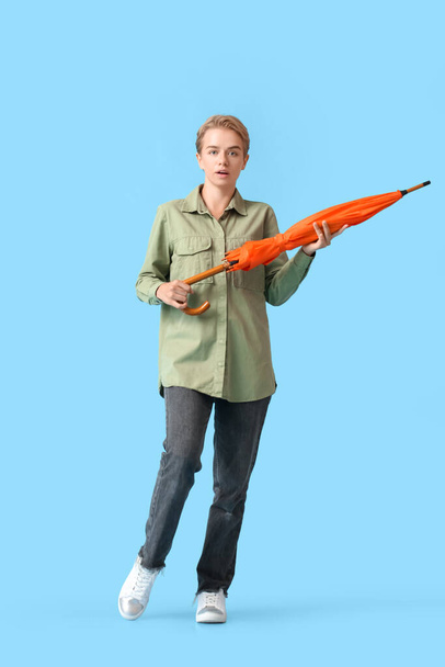 Shocked young woman with orange umbrella on blue background - Foto, afbeelding