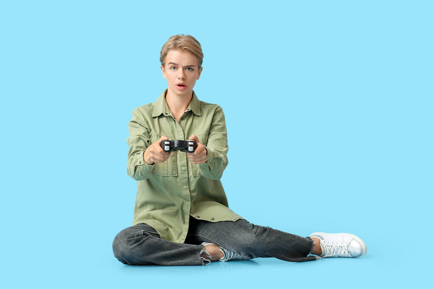 Shocked young woman with game pad on blue background - Photo, Image
