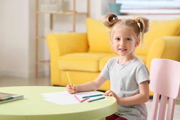 Aranyos kislány lófarokkal rajz az asztalnál a nappaliban - Fotó, kép