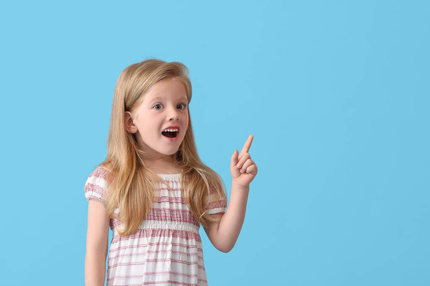 Surprised little girl pointing at something on blue background - Фото, изображение