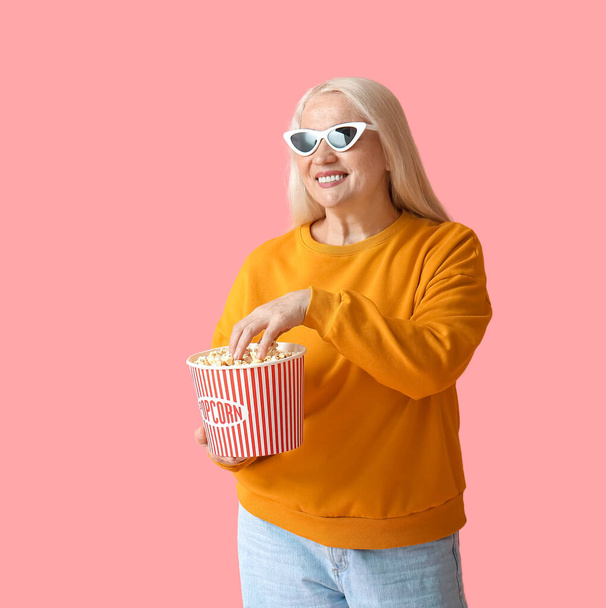 Femme mûre avec du pop-corn savoureux sur fond de couleur - Photo, image