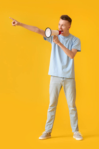 Wütender junger Mann brüllt in Megafon auf gelbem Hintergrund - Foto, Bild