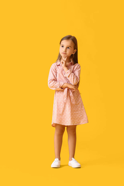 Bedachtzaam klein meisje in jurk op gele achtergrond - Foto, afbeelding