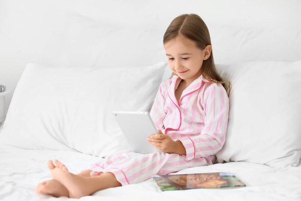 Cute little girl using tablet computer on bed - Фото, изображение