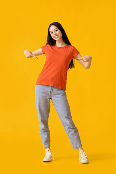 Piękna nastolatka wskazując na pomarańczowy t-shirt na żółtym tle - Zdjęcie, obraz