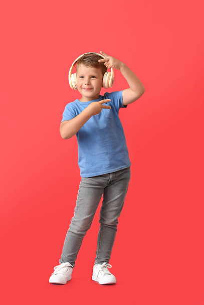 Cute little boy in wireless headphones dancing on red background - Foto, Imagen