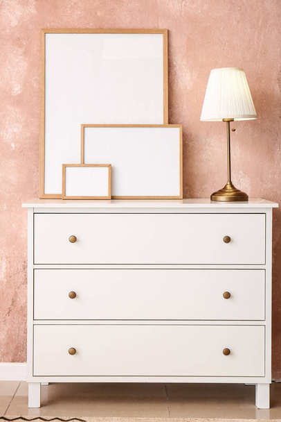 Caixa de gavetas com molduras em branco e lâmpada perto da parede rosa - Foto, Imagem
