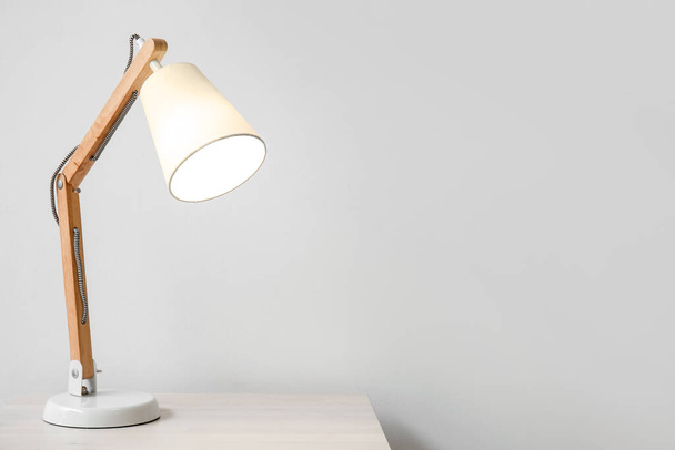 Wooden glowing lamp on table near white wall - Zdjęcie, obraz