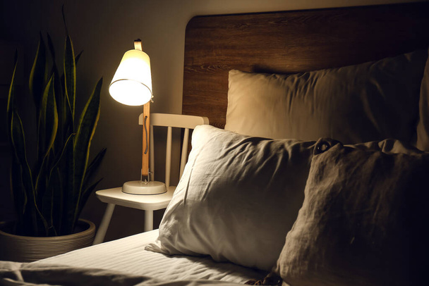 暗い部屋のベッドサイドの椅子に光るランプ - 写真・画像
