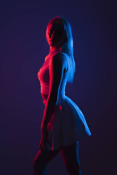 A portrait of a young Canadian woman in sportswear posing under blue and red lights in a dark studio - Фото, зображення