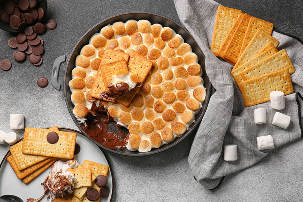 Frying pan with tasty S'mores dip and crackers on grey background - Photo, Image