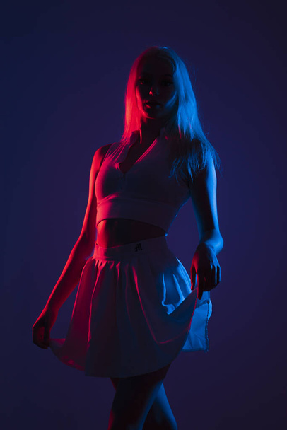 A portrait of a young Canadian woman in sportswear posing under blue and red lights in a dark studio - Foto, Bild