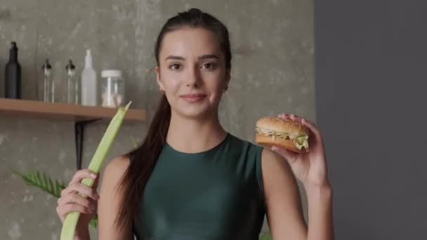 Video of a sporty woman looking at the camera holding a burger and an onion in her hands. Healthy diet - Footage, Video