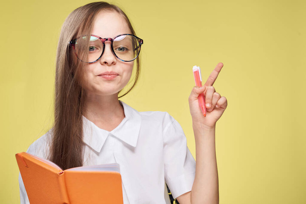 schoolgirl with textbook in hands learning childhood yellow background - Foto, Imagen