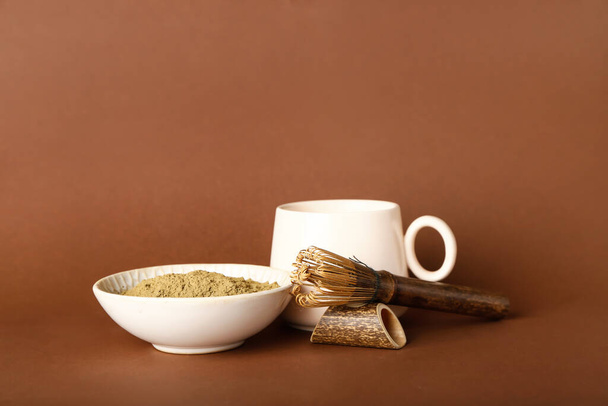 Bowl with hojicha powder, cup of tea and chasen on brown background - Zdjęcie, obraz