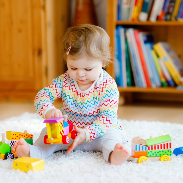 little baby girl playing with educational wooden toys at home or nursery. Toddler with colorful train. Child having fun with different toys. Lonely kid during corona virus pandemic quarantine - Photo, Image