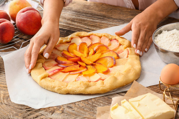 Woman preparing tasty peach galette at table - Photo, Image