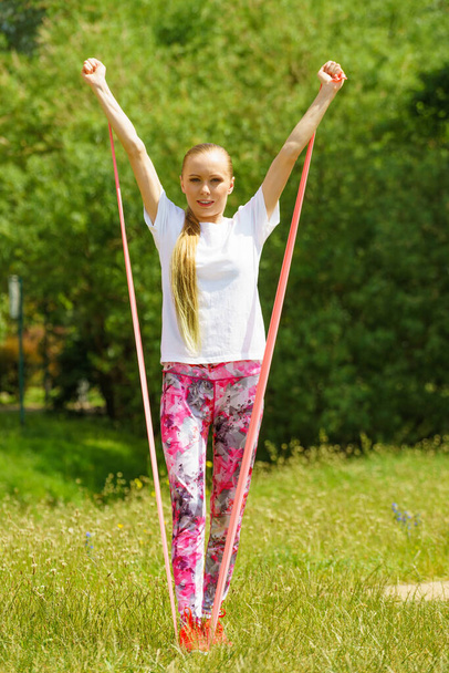 Young woman exercises outdoor in park, using gym accessory, resistance band. Staying fit and healthy. - Foto, Imagem