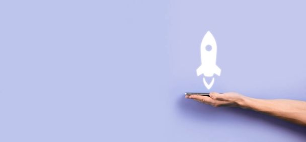 Мужчина держит иконку ракеты, которая взлетает, запуск на синем фоне. ракета запускается и летит, бизнес-старт, маркетинг иконок на современном виртуальном интерфейсе. Концепция стартапа - Фото, изображение