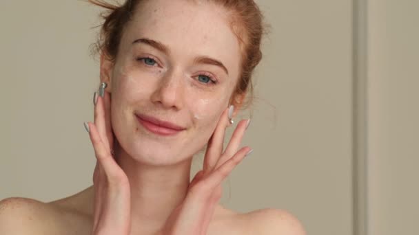 Video with a woman with red hair and freckles, spreading her cream with her hands all over her face. Facial care - Footage, Video