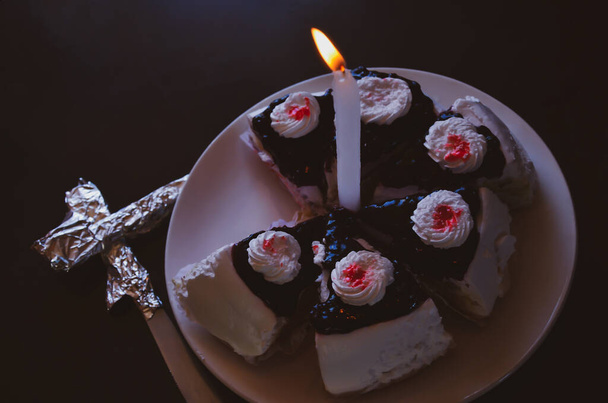 ホワイトバニラ風味のケーキとダークチョコレートのスライスの夜景は、中央のプレートと照明のろうそくに白と赤のクリームをトッピング。誕生日やバレンタインパーティーのための自家製パンケーキ - 写真・画像