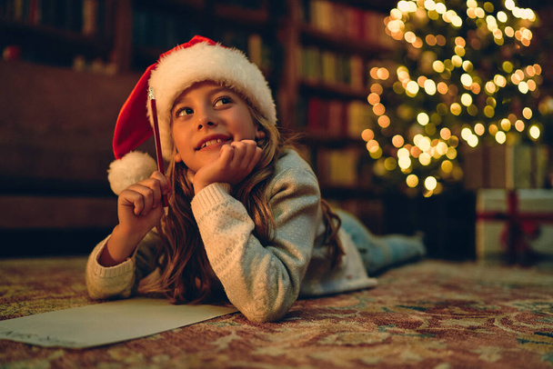 Веселого Різдва і щасливих свят! Мила дівчинка пише листа Санта Клаусу біля ялинки.. - Фото, зображення