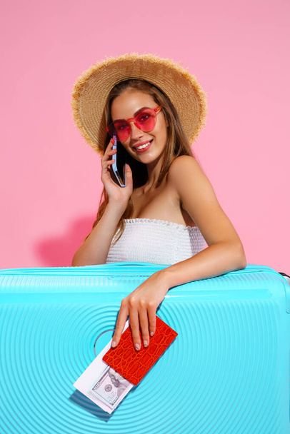Happy girl in summer clothes with baggage holds ticket, passport, money while talking on the phone - Zdjęcie, obraz