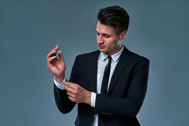 portrait d'un homme tendance, séduisant et magnifique en smoking noir avec bouton cravate sur les poignets de sa chemise blanche, isolé sur fond gris. - Photo, image