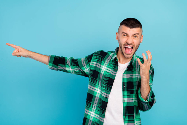 Photo of unhappy upset young angry man point finger empty space scream isolated on blue color background - Photo, Image