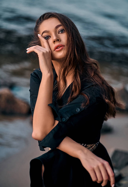 Close-up portret van een mooie jonge brunette met lang haar poserend op het strand bij zonsondergang. Genieten van de natuur. - Foto, afbeelding