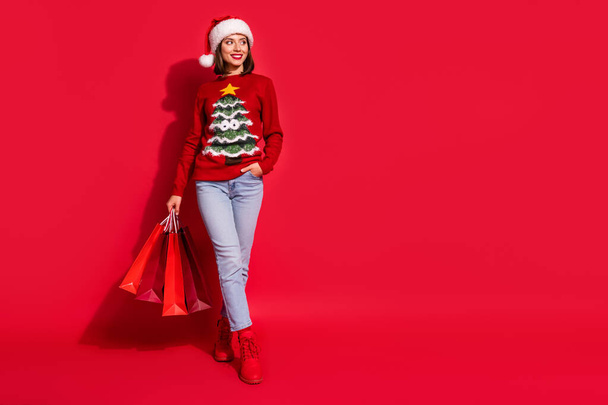 Photo of dreamy pretty lady dressed print pullover smiling walking holding noel bargains looking empty space isolated red color background - Foto, Imagem