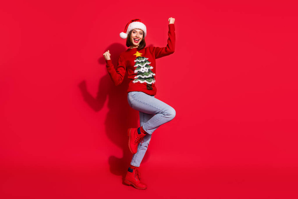 Photo of lucky funny young woman wear print sweater rising fists celebrating new year isolated red color background - Fotoğraf, Görsel