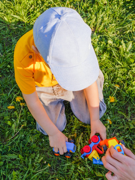 Boy plays with a toy car on the green grass lawn in park - Zdjęcie, obraz