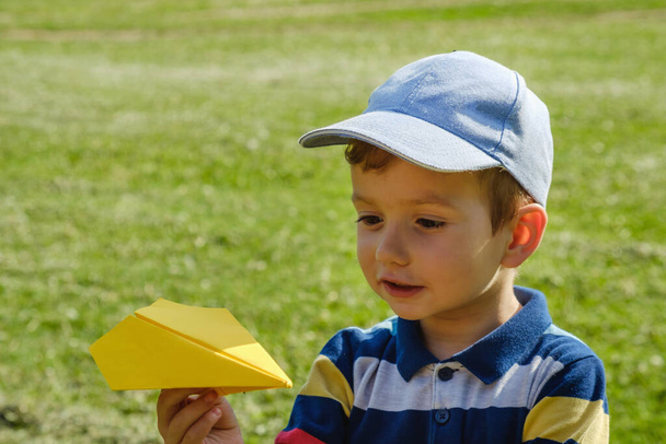 Boy playing with a yellow toy plane at park on a sunny summer day - Fotó, kép