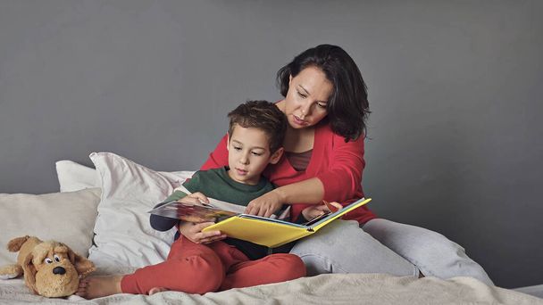 mother and son reading book together on bed - 写真・画像