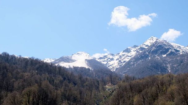 beautiful landscape of snow-capped mountains with white clouds on blue sky on a sunny day at Krasnaya Polyana in Sochi, Russia. Famous ski resort - Фото, зображення