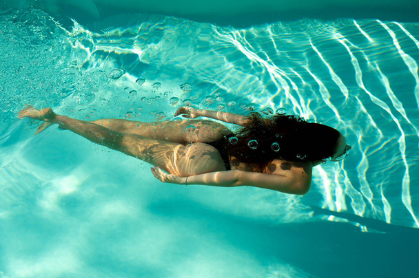 Woman swimming underwater in a blue pool - Fotoğraf, Görsel