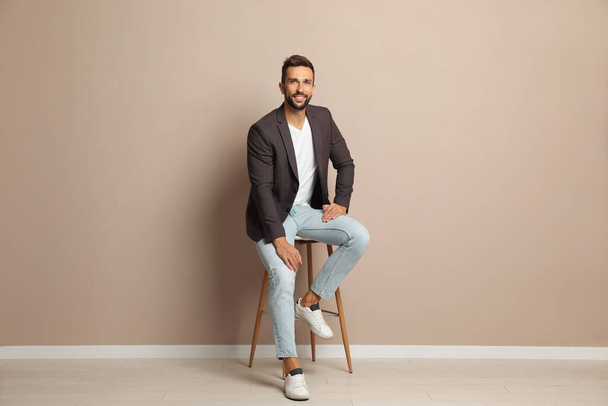 Handsome man sitting on stool near beige wall - Foto, imagen