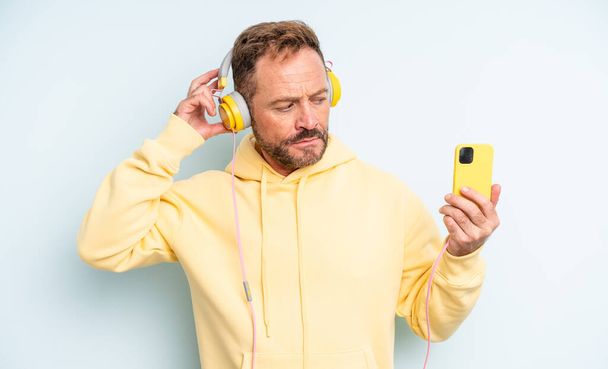 middle age handsome man smiling happily and daydreaming or doubting. headphones and smartphone concept - Φωτογραφία, εικόνα