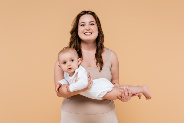 Cheerful plus size woman holding baby daughter isolated on beige  - Photo, Image