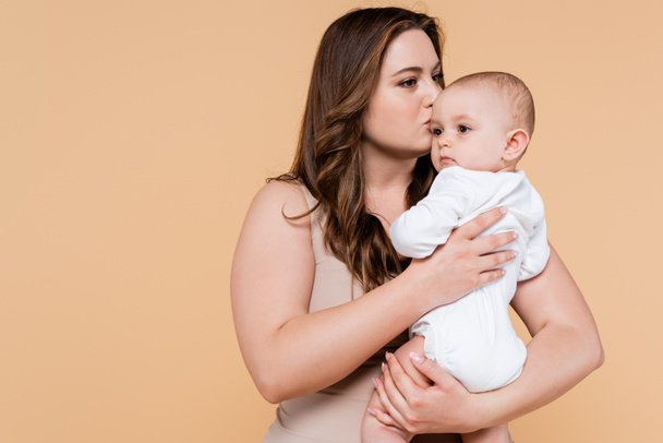 Plus size mother kissing baby daughter isolated on beige  - Photo, Image