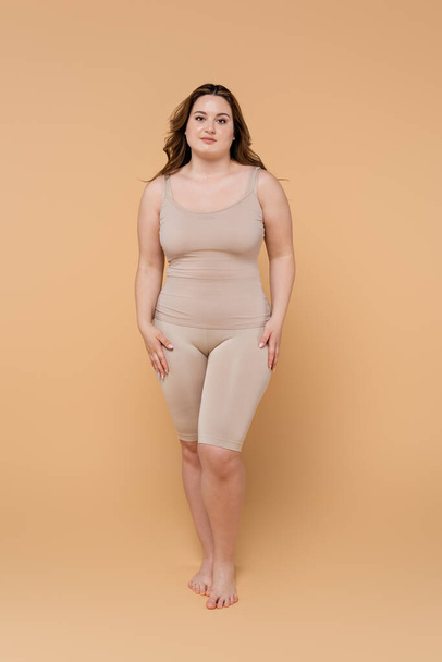 Full length of barefoot plus size woman looking at camera on beige background  - Foto, Imagem