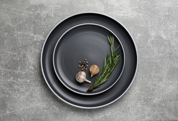 New dark plates with rosemary, garlic and peppercorns on light grey table, top view - Foto, afbeelding